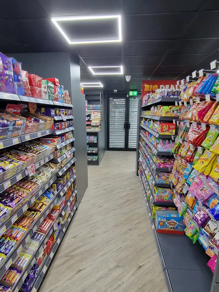 Black suspended ceiling with square LED light fittings above shop aisles